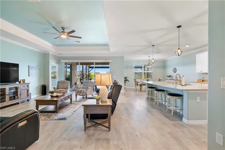 Living area with ornamental molding, ceiling fan, light wood finished floors, suspended lighting, and a raised ceiling