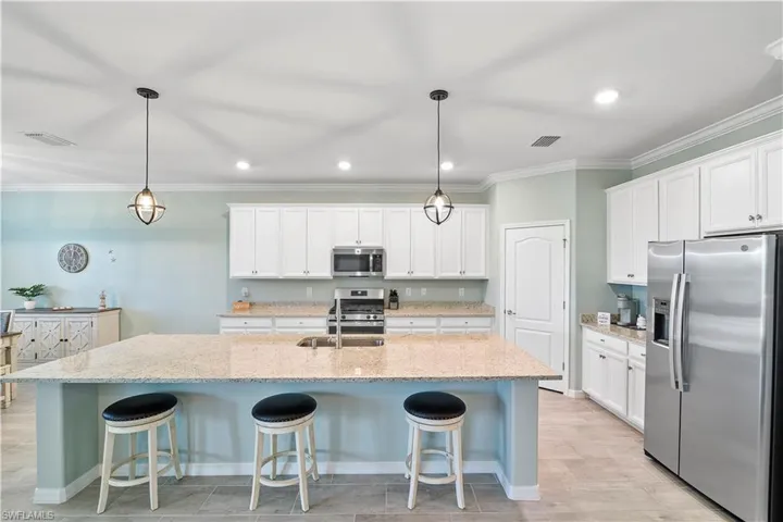 Kitchen with a kitchen bar, stainless steel appliances, ornamental molding, an island with sink, and light stone countertops