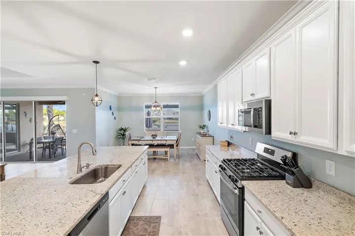 Kitchen with stainless steel appliances, white cabinets, light stone countertops, crown molding, and a chandelier