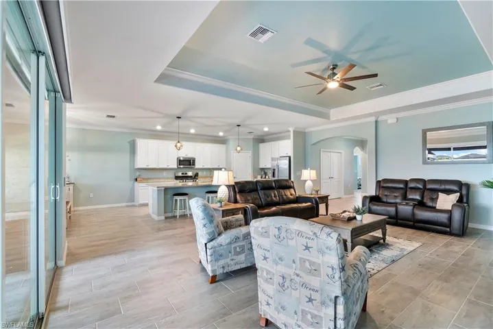 Living room featuring arched walkways, ornamental molding, ceiling fan, a tray ceiling, and wood tiled floors