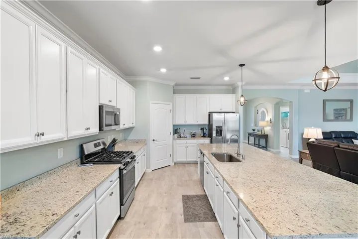 Kitchen featuring arched walkways, stainless steel appliances, white cabinets, a large island, and ornamental molding
