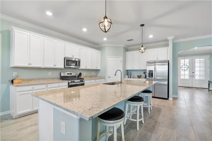 Kitchen featuring arched walkways, stainless steel appliances, white cabinets, light stone countertops, and a breakfast bar area