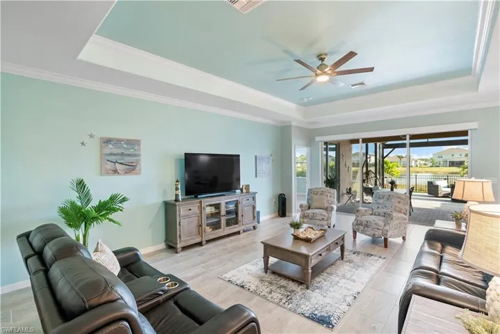 Living area with a ceiling fan, ornamental molding, a raised ceiling, and wood finish floors