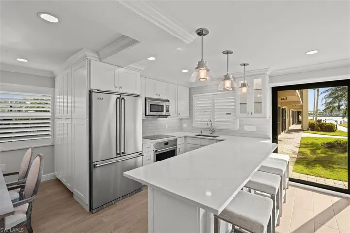 Kitchen featuring ornamental molding, appliances with stainless steel finishes, white cabinetry, pendant lighting, and a kitchen breakfast bar