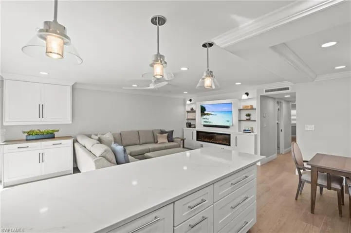 Kitchen featuring ornamental molding, white cabinetry, light stone counters, light wood-type flooring, and a glass covered fireplace