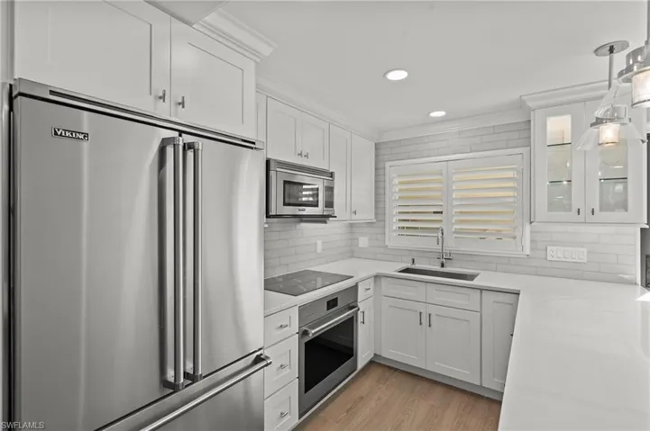 Kitchen featuring appliances with stainless steel finishes, white cabinets, glass insert cabinets, ornamental molding, and light wood finished floors