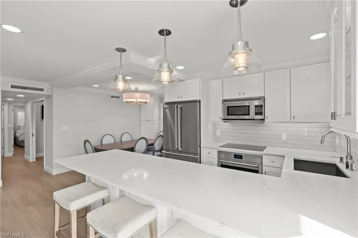 Kitchen featuring light stone countertops, white cabinets, appliances with stainless steel finishes, a peninsula, and backsplash