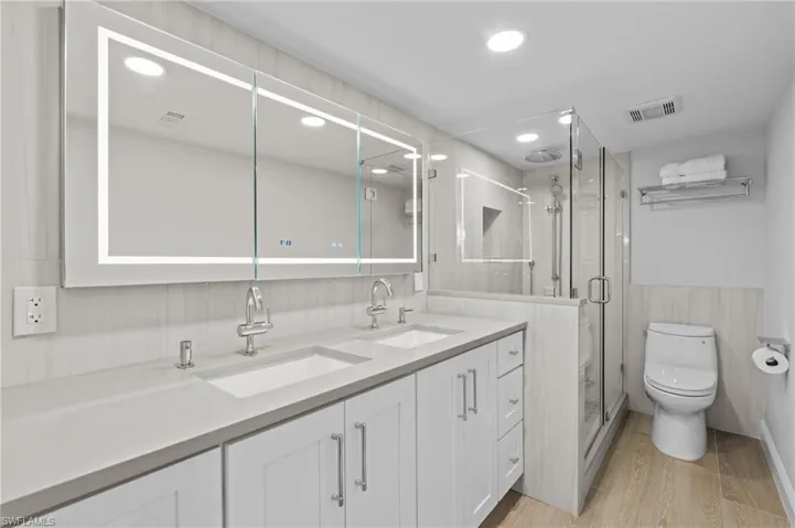 Bathroom with light wood finished floors, double vanity, a shower stall, recessed lighting, and a wainscoted wall