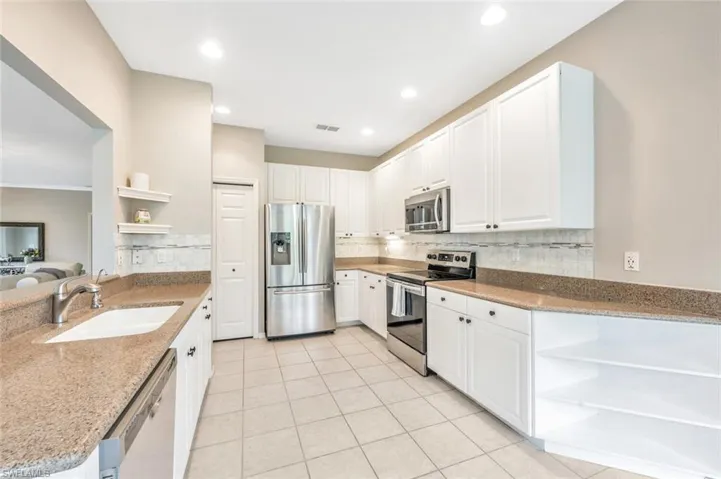 Kitchen featuring light stone counters, sink, white cabinetry, stainless steel appliances, and decorative backsplash