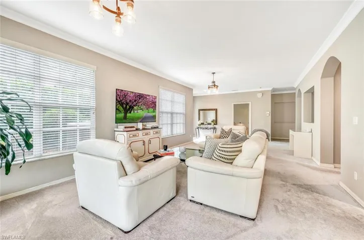 Carpeted living room featuring crown molding and a chandelier