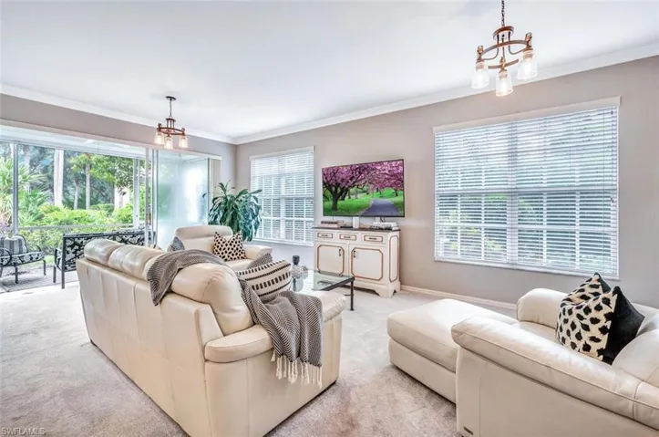 Living room with light carpet, ornamental molding, a chandelier, and a wealth of natural light