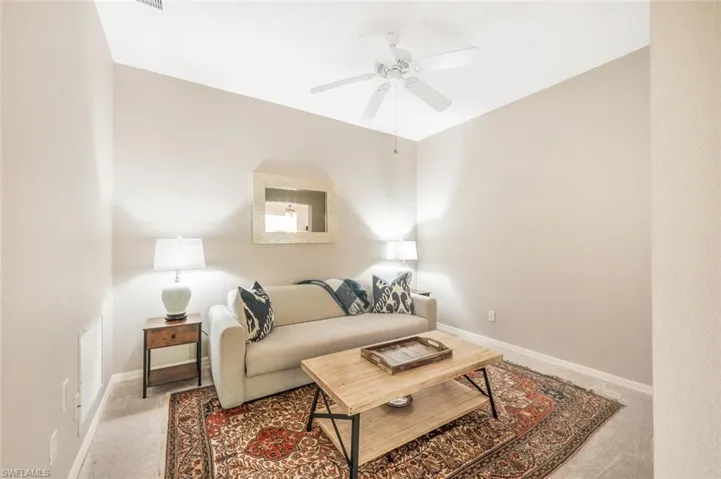 Den with light carpet and ceiling fan