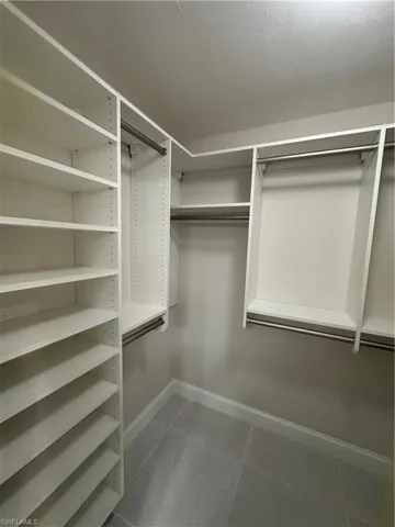 Built-in custom closet system featuring white shelving, multiple hanging rods, and tile flooring