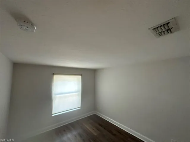 Wood-finish flooring with white baseboards, a window with roller shade, and a textured ceiling