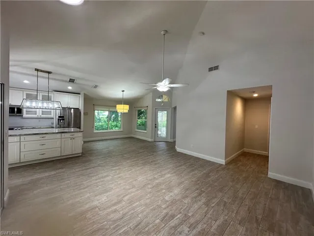 Open-concept living space featuring vaulted ceilings, wood-finish flooring, a kitchen island with stone countertops, white shaker cabinetry, and a ceiling fan