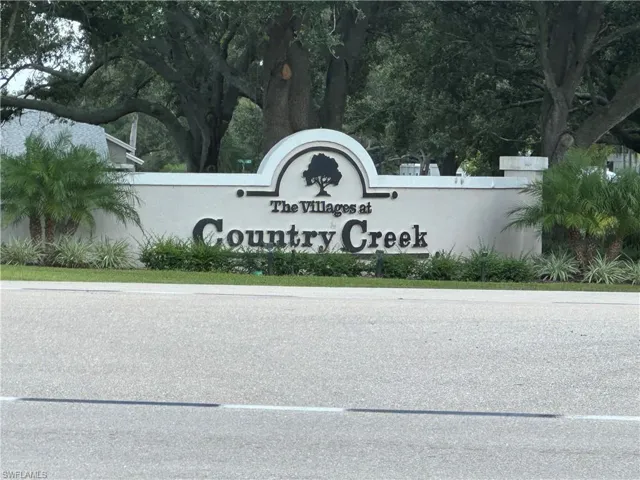 Community entry monument with "The Villages at Country Creek" signage, surrounded by mature trees and landscaping