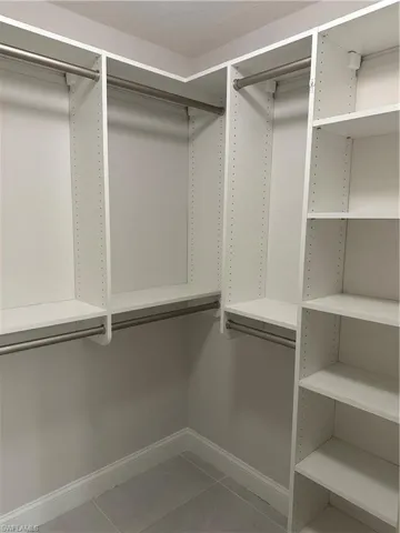Built-in white custom closet system featuring multiple hanging rods, adjustable shelving, and tile flooring