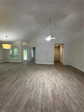 Vaulted ceilings, wood-finish flooring, ceiling fan, pendant light fixture, and transom window above the entry door