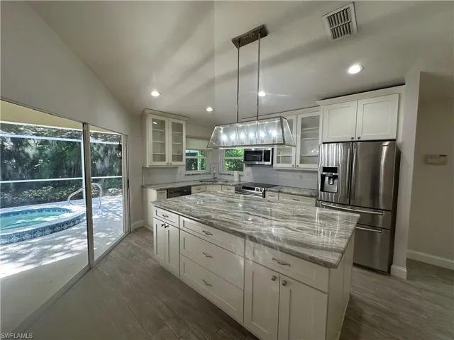 Vaulted ceiling kitchen featuring an expansive center island with stone countertop, stainless steel appliances, and wood-finish flooring