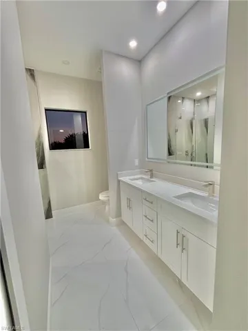 Bathroom featuring double vanity, light marble finish floors, a marble finish shower, and recessed lighting