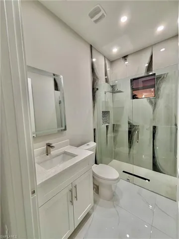 Full bath with vanity, a marble finish shower, light marble finish flooring, and recessed lighting