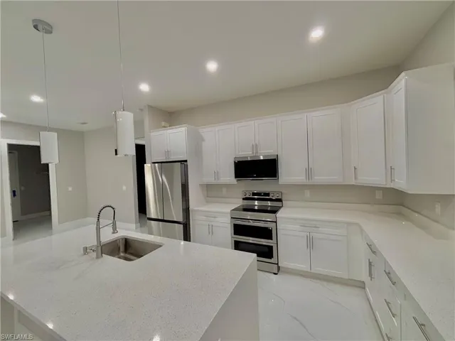 Kitchen with stainless steel appliances, light stone countertops, white cabinetry, recessed lighting, and pendant lighting