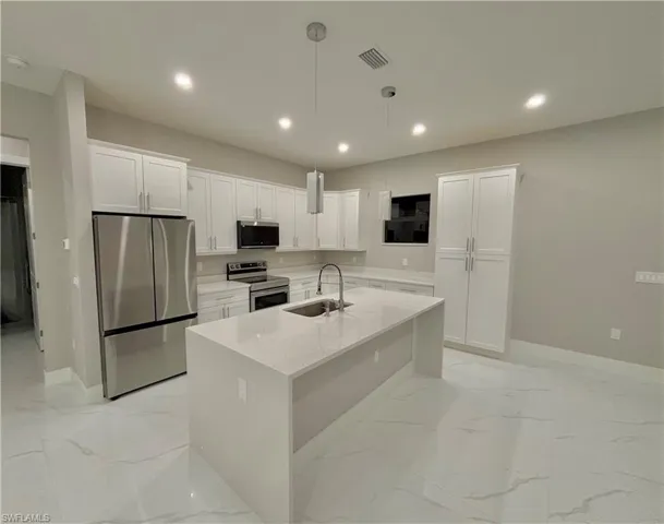 Kitchen featuring appliances with stainless steel finishes, white cabinetry, light stone countertops, hanging light fixtures, and light marble finish floors