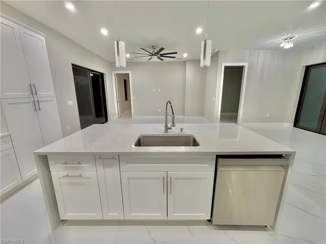 Kitchen featuring hanging light fixtures, light stone counters, dishwasher, a large island with sink, and recessed lighting