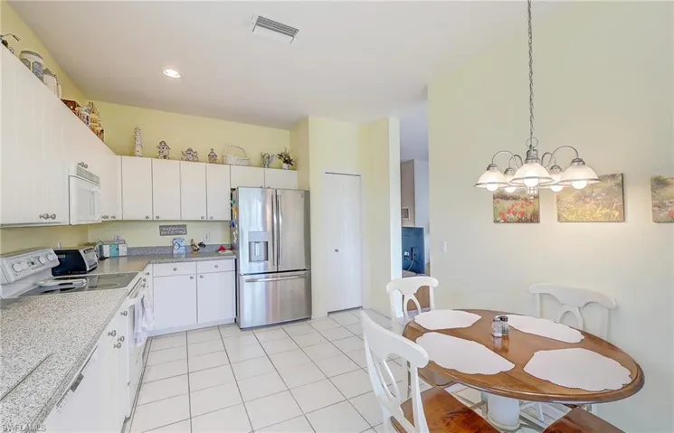 Kitchen with white appliances, light countertops, white cabinetry, light tile patterned flooring, and a chandelier