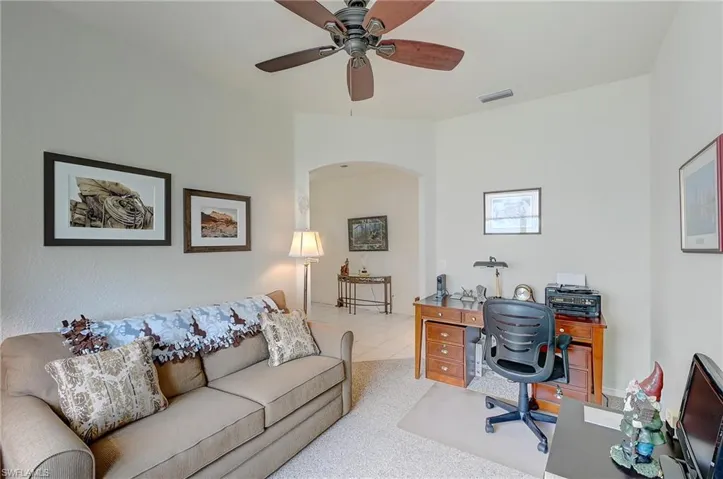 Office area featuring a ceiling fan, arched walkways, and light carpet