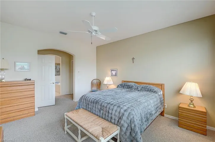 Bedroom featuring light colored carpet, arched walkways, and ceiling fan