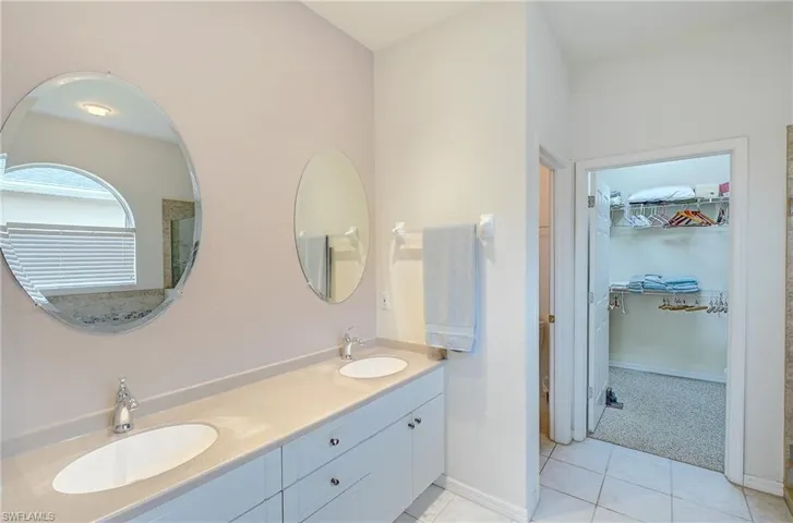 Bathroom featuring a walk in closet, double vanity, light carpet, and light tile patterned floors