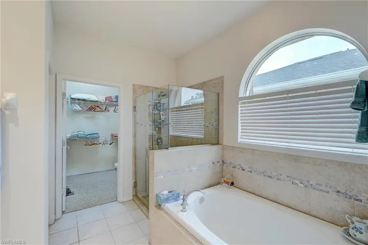 Full bathroom with a walk in closet, a shower stall, a garden tub, light tile patterned flooring, and light carpet