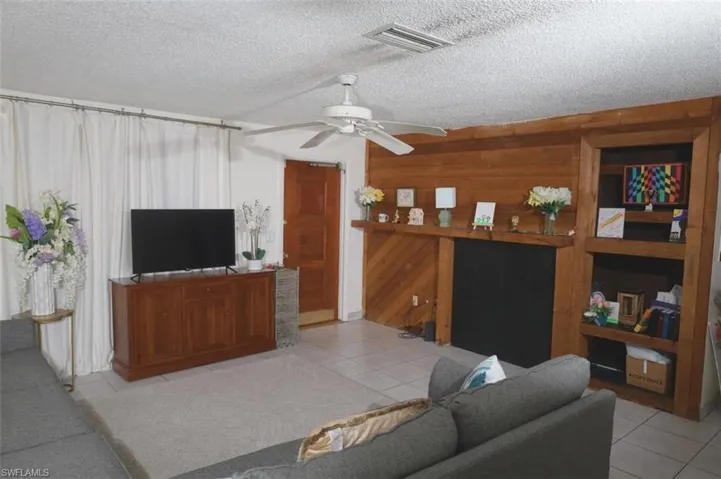 Tiled living room with a ceiling fan, a textured ceiling, and wood walls