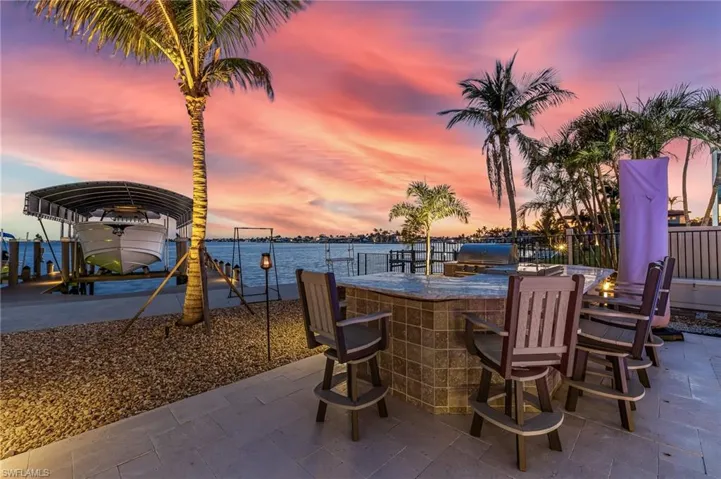 Patio terrace at dusk with outdoor wet bar, a dock, a water view, boat lift, and exterior kitchen