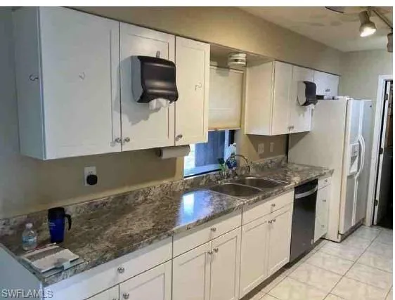 Kitchen featuring laminate counters, dishwasher, light tile floors, sink, and white cabinetry
