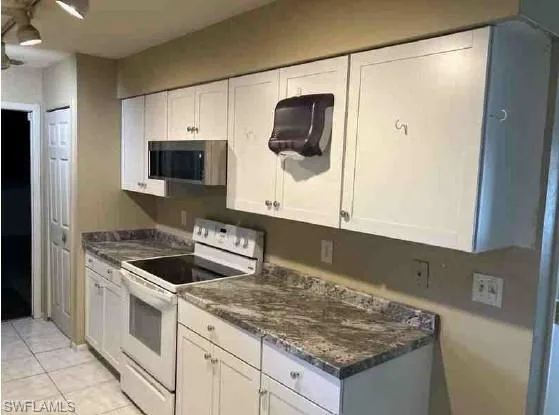Kitchen featuring electric stove, cabinets, light tile flooring, and laminate countertops