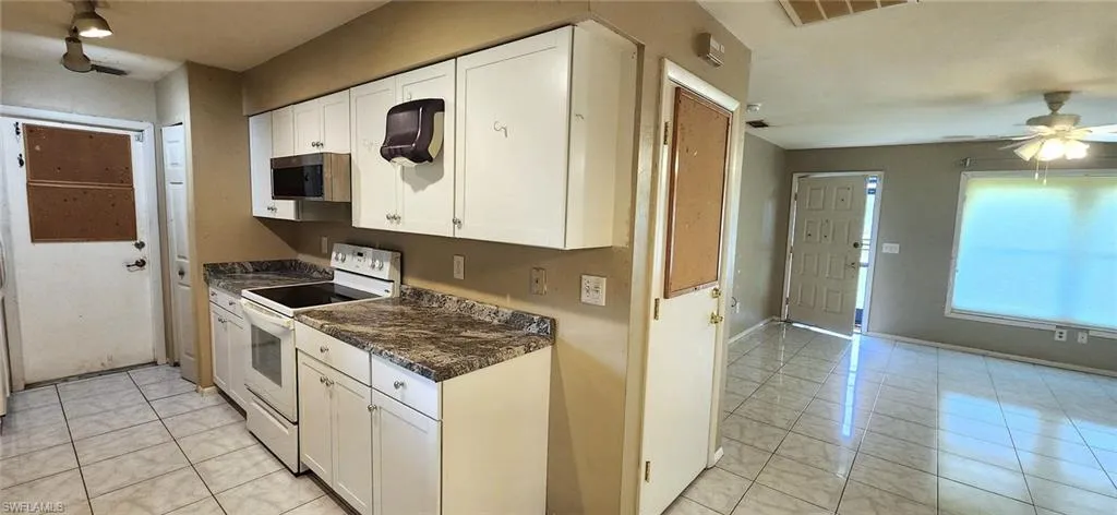 Kitchen featuring light tile patterned floors, ceiling fan, dark stone counters, white cabinetry, and white range with electric stovetop