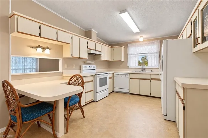 Kitchen featuring white appliances, cream cabinetry, a built-in dining counter, and wood-finish flooring