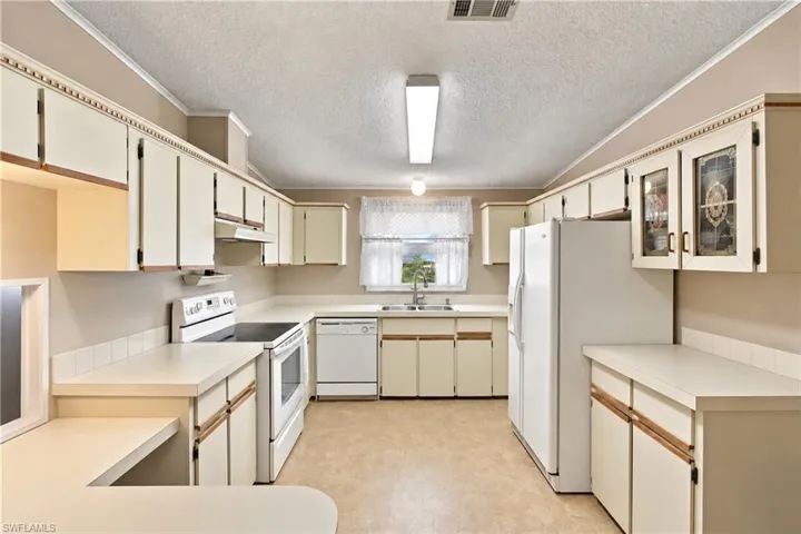 U-shaped kitchen featuring white cabinetry, light countertops, white appliances, and a window above the sink