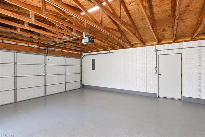 Spacious garage with exposed wood ceiling beams, white sectional garage door, light grey flooring, and an additional white entry door