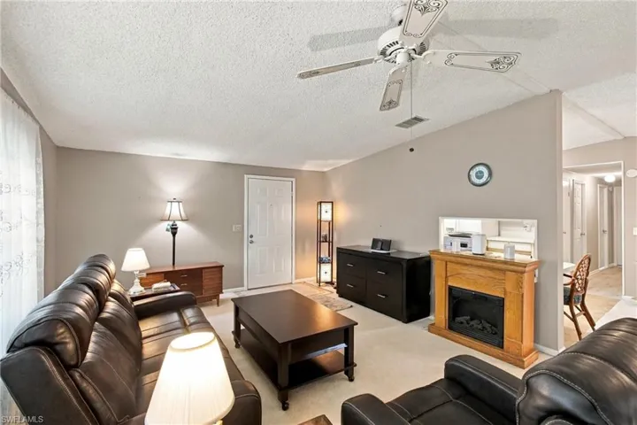 Living area featuring a ceiling fan, light-colored carpeting, a partial room divider, and a decorative fireplace