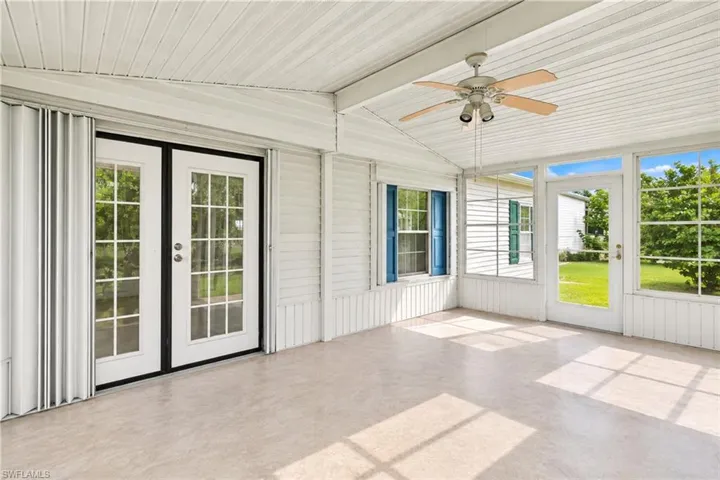 Enclosed patio with a ceiling fan, multiple windows with blue shutters, a glass-paneled entry door, and a second set of glass-paned doors