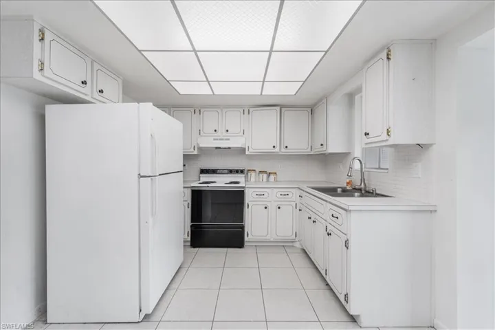 Kitchen with freestanding refrigerator, light countertops, range with electric cooktop, and white cabinetry