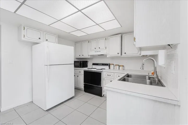 Kitchen with white appliances, light countertops, white cabinets, and tasteful backsplash