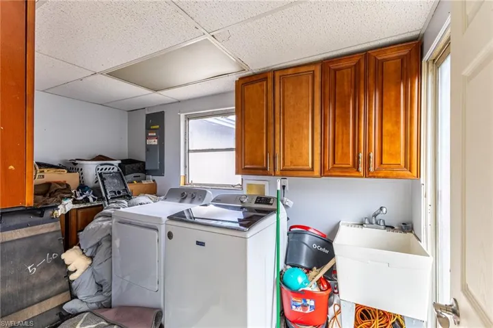Laundry area featuring cabinet space, electric panel, washer and clothes dryer, and a sink