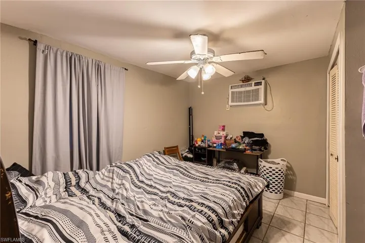 Bedroom featuring ceiling fan, light tile patterned flooring, baseboards, and a wall mounted air conditioner