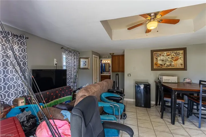 Living room with a ceiling fan, a tray ceiling, light tile patterned flooring, and baseboards