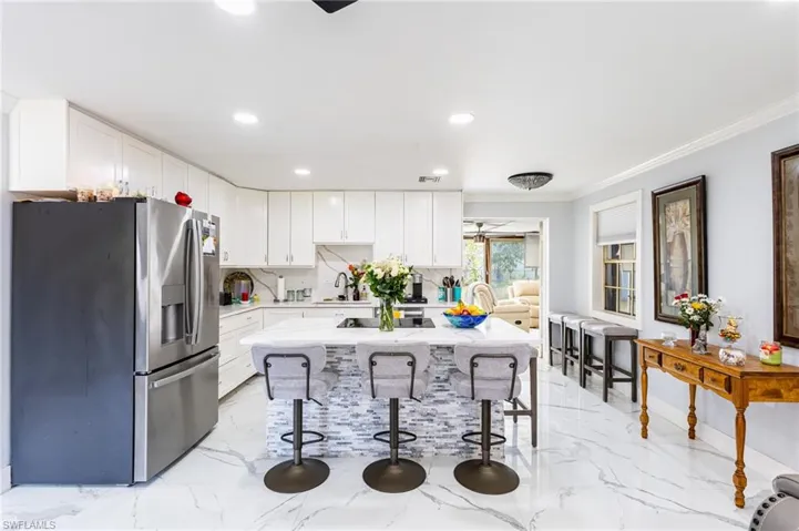 Kitchen with a breakfast bar, marble finish floor, crown molding, backsplash, and stainless steel fridge with ice dispenser