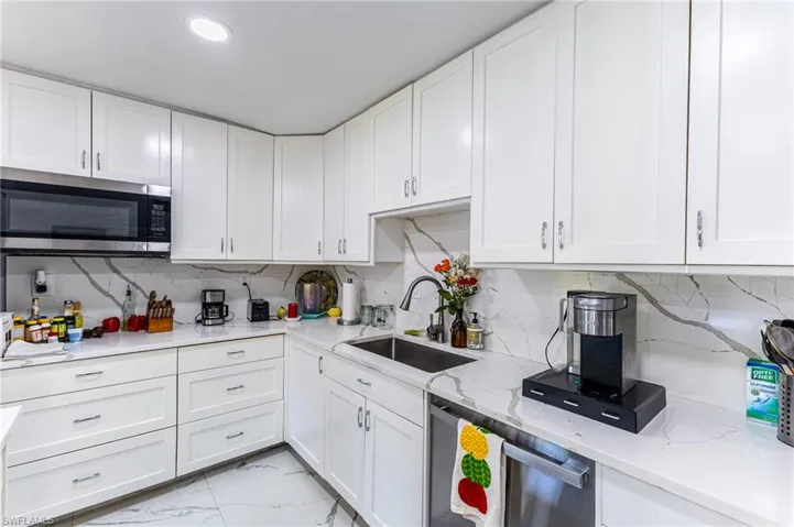 Kitchen featuring stainless steel appliances, a sink, white cabinets, marble finish floor, and light stone countertops